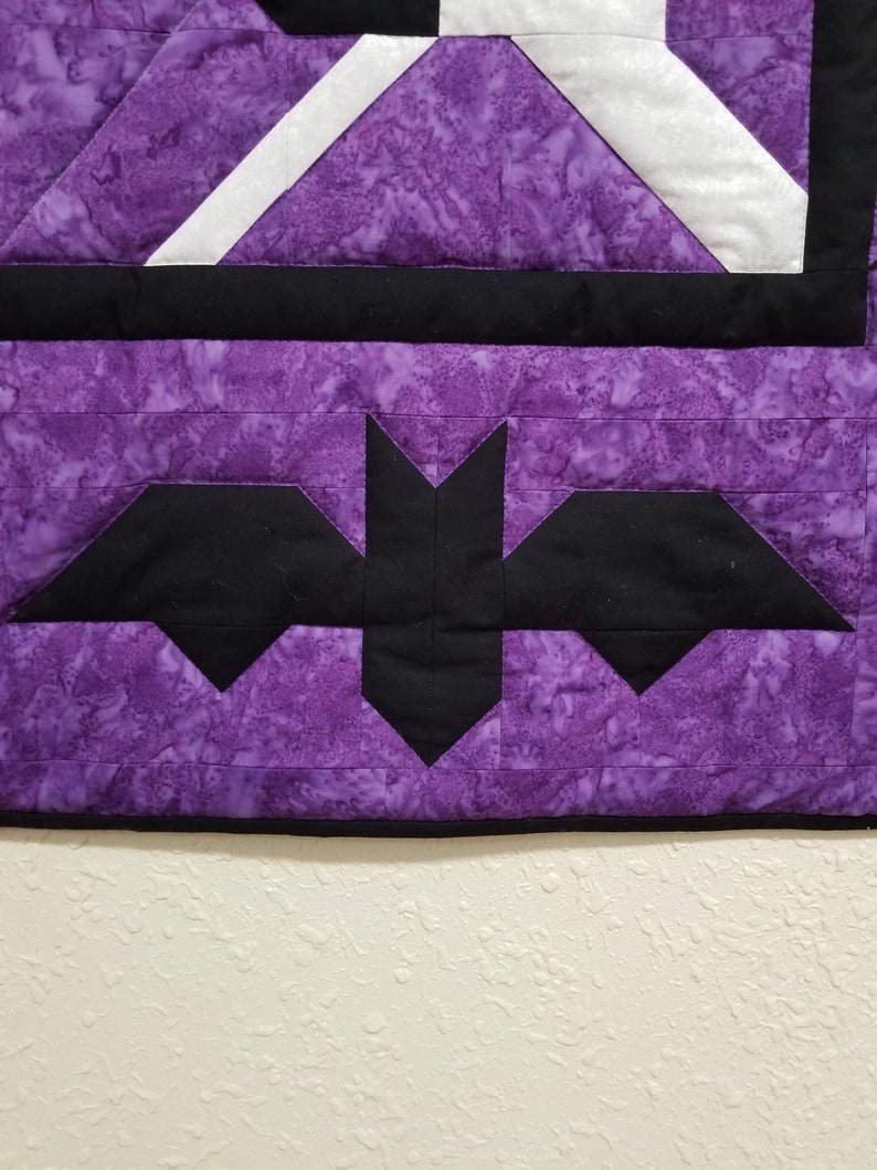 May include: Purple and black quilt with a bat design. The quilt is made of fabric with a marbled pattern.