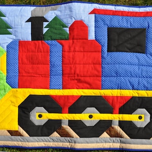 May include: A colourful patchwork quilt featuring a train design. The train is made of red, blue, yellow, and black fabric. The quilt is perfect for a child's room.