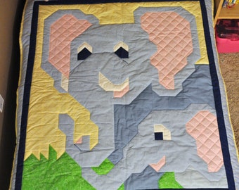 May include: A blue and pink patchwork quilt featuring a large elephant with a smaller elephant in its trunk. The quilt has a yellow background with green grass at the bottom.