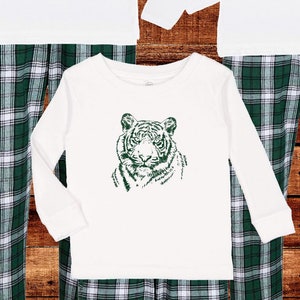 May include: White long-sleeve shirts and green plaid pajama pants. Each shirt features a green tiger graphic. The text on the image says "High-quality, soft, and long-lasting shirts and inks" and "Designed and printed by hand in our Midwestern studio."