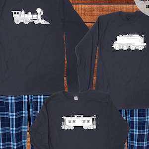 Può includere: Tre camicie a maniche lunghe con un motivo a quadri blu e bianchi. Le camicie presentano un contorno bianco di un locomotore su uno sfondo blu scuro. Il testo "Ships next day!" e "sunshine mountain tees" è visibile nella parte superiore e inferiore dell'immagine. Il testo "High-quality, soft, and long-lasting shirts and inks" è visibile nell'angolo in alto a destra dell'immagine. Il testo "Designed and printed by hand in our Midwestern studio" è visibile nell'angolo in basso a sinistra dell'immagine.