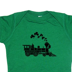 May include: A green baby onesie with a black silhouette of a train with shamrocks coming out of the smoke stack.