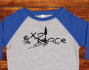 May include: A gray and blue raglan style t-shirt with the word "Explore" in black script. The design includes a mountain, tent, and tree graphic. The shirt has three-quarter length sleeves.