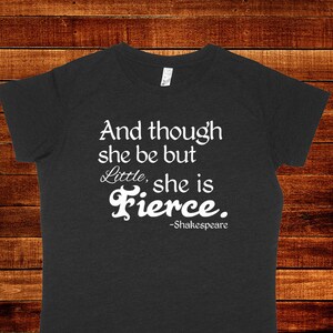 Può includere: Una maglietta grigia scura con testo bianco che recita "And though she be but little, she is Fierce. -Shakespeare".