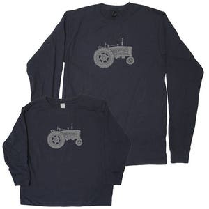Pu&ograve; includere: Un set di due magliette a maniche lunghe blu navy con una silhouette grigia di un trattore. La maglietta pi&ugrave; piccola &egrave; per un bambino e la maglietta pi&ugrave; grande &egrave; per un adulto.