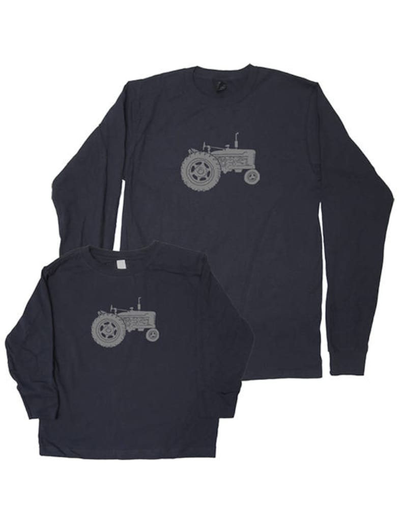Pu&ograve; includere: Un set di due magliette a maniche lunghe blu navy con una silhouette grigia di un trattore. La maglietta pi&ugrave; piccola &egrave; per un bambino e la maglietta pi&ugrave; grande &egrave; per un adulto.