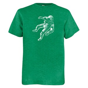 May include: A green t-shirt with a white illustration of an astronaut in a spacesuit. The astronaut is depicted floating. The t-shirt has a crew neck and short sleeves. The fabric has a textured appearance.