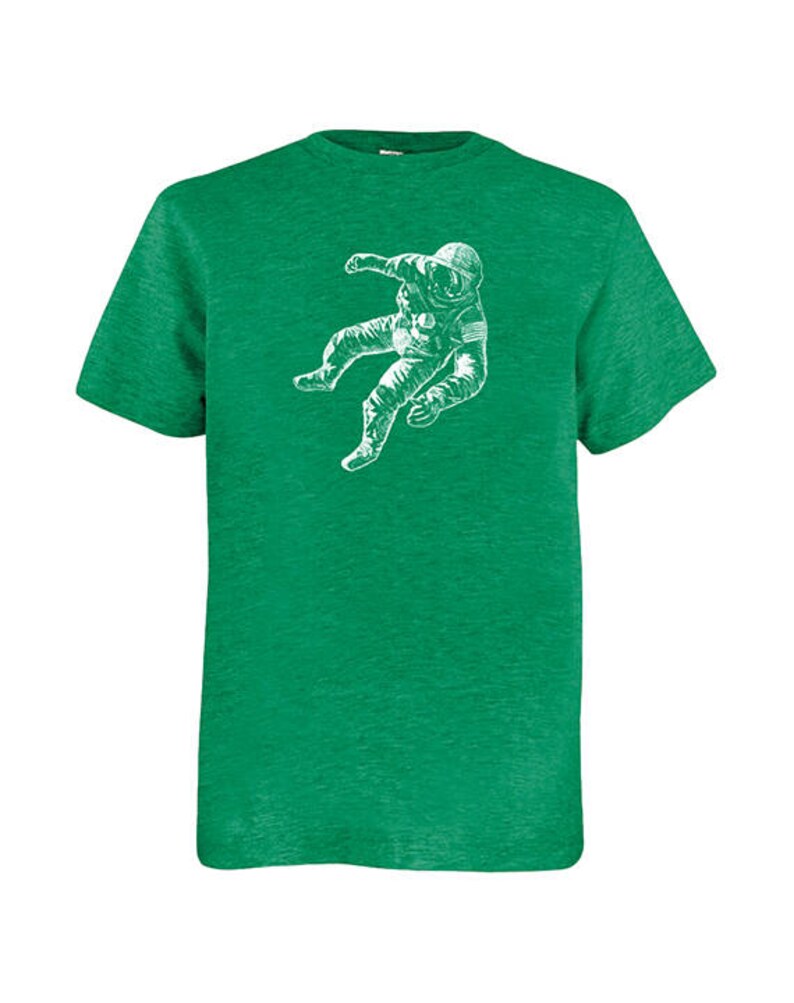 May include: A green t-shirt with a white illustration of an astronaut in a spacesuit. The astronaut is depicted floating. The t-shirt has a crew neck and short sleeves. The fabric has a textured appearance.