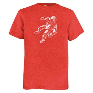 May include: Red t-shirt with a white graphic of an astronaut floating in space. The astronaut is wearing a spacesuit and helmet. The t-shirt has short sleeves and is made of a soft fabric.