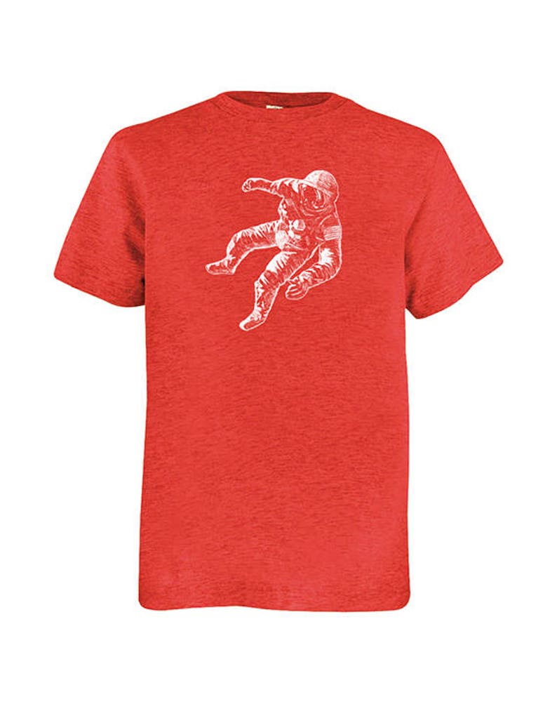 May include: Red t-shirt with a white graphic of an astronaut floating in space. The astronaut is wearing a spacesuit and helmet. The t-shirt has short sleeves and is made of a soft fabric.