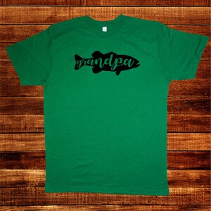 May include: Green t-shirt with a black silhouette of a fish and the word "grandpa" written in cursive.