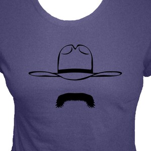 May include: A purple t-shirt with a black silhouette of a cowboy hat and mustache.