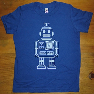 May include: A royal blue t-shirt with a white robot graphic. The robot has a round head with two eyes, a rectangular body with a screen and buttons, and two arms and legs.