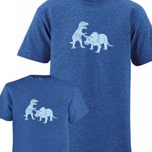 Puede incluir: Dos camisetas azules con un gr&aacute;fico de un dinosaurio luchando contra un triceratops. El gr&aacute;fico es de color azul claro.