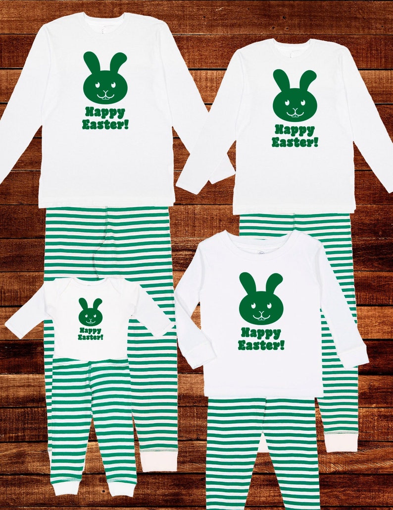 Może przedstawiać: Zestaw czterech białych piżam w zielone paski z zielonym nadrukiem kr&oacute;lika. Piżamy mają napis "Wesołych Świąt Wielkanocnych!" z przodu.