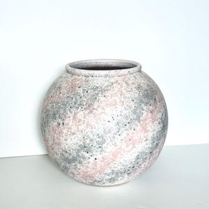 May include: A set of three ceramic mugs with a speckled, matte finish. The mugs are in shades of cream, light gray, and dark gray. Each mug has a simple, minimalist design and a rounded handle.