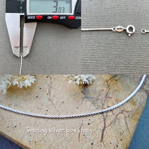 May include: A close-up of a silver box chain necklace. The chain is 3.03 mm wide. The necklace is on a light brown surface.