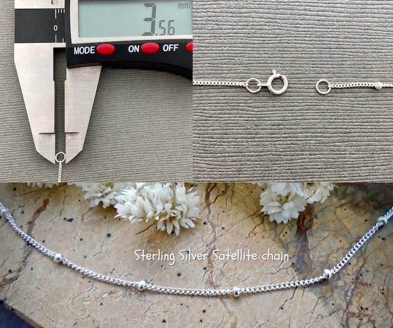 May include: A close-up of a silver satellite chain necklace with small round beads. The chain is 3.56 mm wide. The necklace is shown on a textured surface with white flowers.
