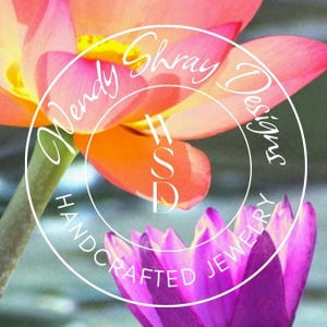 Puede incluir: Primer plano de un vibrante arreglo floral con una flor de loto rosa y naranja y una flor de loto p&uacute;rpura en primer plano. La imagen tiene un logotipo circular blanco con el texto "Wendy Shray Designs" y "Handcrafted Jewelry".