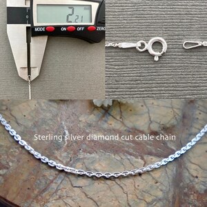 May include: A close-up of a silver diamond cut cable chain necklace. The chain is 2.21 mm wide and is shown next to a ruler. The chain is also shown laid out on a textured surface.