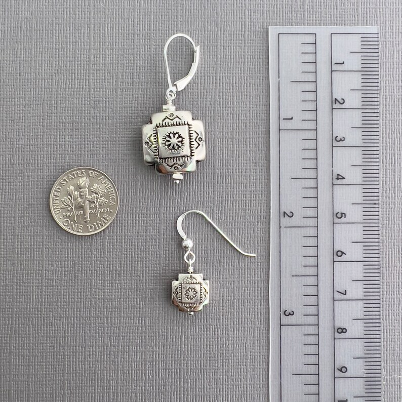 May include: A pair of silver earrings with a geometric design. The larger earring is about 1 inch long and the smaller earring is about 1/2 inch long. The earrings are shown next to a ruler for size reference.