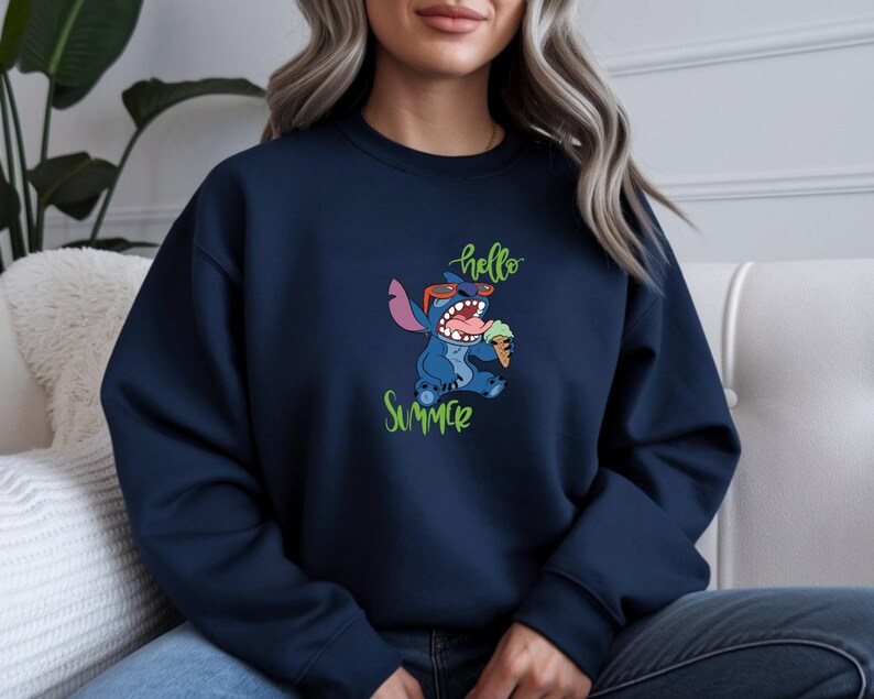 Puede incluir: Sudadera azul marino con un dise&ntilde;o de Stitch, el personaje de dibujos animados, con gafas de sol y helado. Las palabras "hello Summer" est&aacute;n escritas en verde arriba y abajo. La sudadera es de cuello redondo.