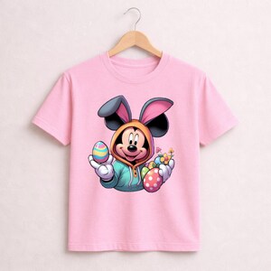 May include: Pink t-shirt featuring a cartoon Mickey Mouse character dressed as the Easter Bunny. Mickey is holding colorful Easter eggs and flowers. The shirt has a crew neck and short sleeves.