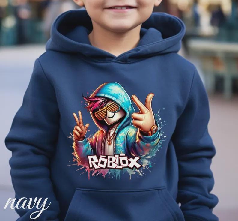 Puede incluir: Sudadera con capucha azul marino con un gr&aacute;fico colorido de un personaje con gafas de sol haciendo el signo de la paz. La palabra "ROBLOX" se muestra en una fuente vibrante y multicolor. La sudadera tiene una capucha con cord&oacute;n y un bolsillo delantero.