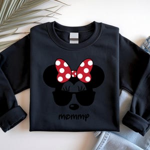 Może przedstawiać: Czarna bluza z nadrukiem Myszki Minnie w okularach przeciwsłonecznych i czerwoną kokardą w białe grochy. Poniżej nadrukowano słowo "mommy". Bluza jest prezentowana na białej powierzchni.