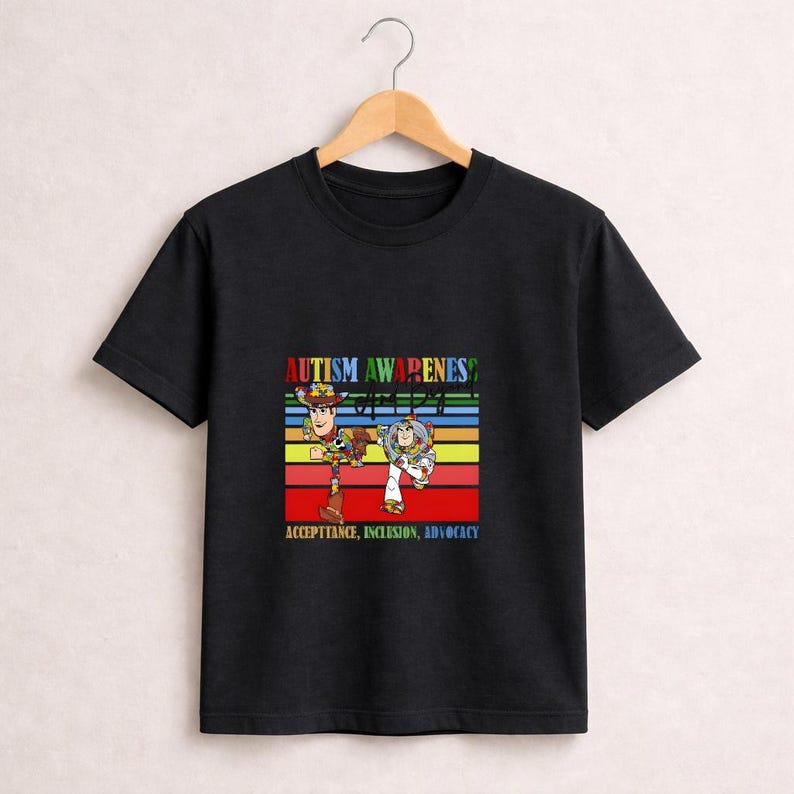 May include: Black t-shirt featuring a colorful graphic with the text "AUTISM AWARENESS" and the words "ACCEPTANCE, INCLUSION, ADVOCACY". The graphic includes cartoon characters on a striped background.