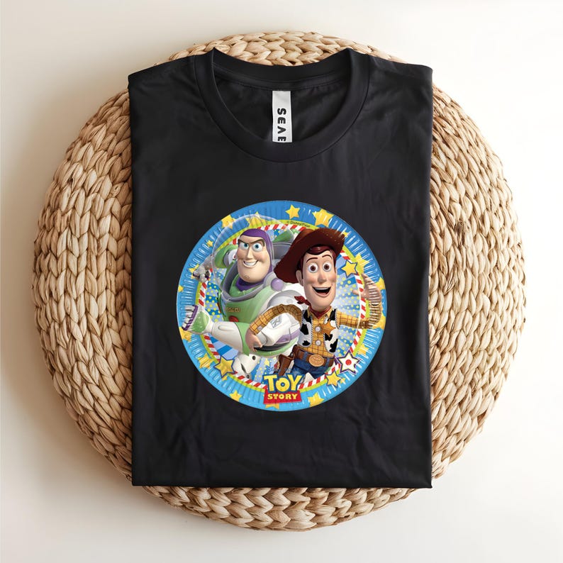 Puede incluir: Camiseta negra con un gr&aacute;fico circular colorido de Buzz Lightyear y Woody de Toy Story. El gr&aacute;fico est&aacute; rodeado por un borde azul con estrellas amarillas y las palabras "Toy Story".