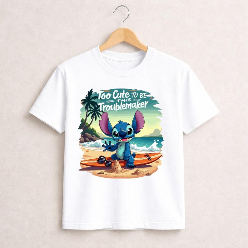 Pu&ograve; includere: T-shirt bianca con un personaggio dei cartoni animati su una tavola da surf sulla spiaggia. Il personaggio blu ha grandi orecchie e sorride. Il testo "Too Cute to Be This Troublemaker" &egrave; sopra il personaggio.