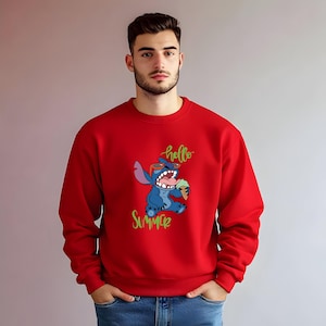 Puede incluir: Una sudadera roja con un dise&ntilde;o de personaje de dibujos animados azul. El personaje lleva gafas de sol y sostiene un helado. Las palabras "hello summer" est&aacute;n escritas en verde. La sudadera es de color rojo liso.