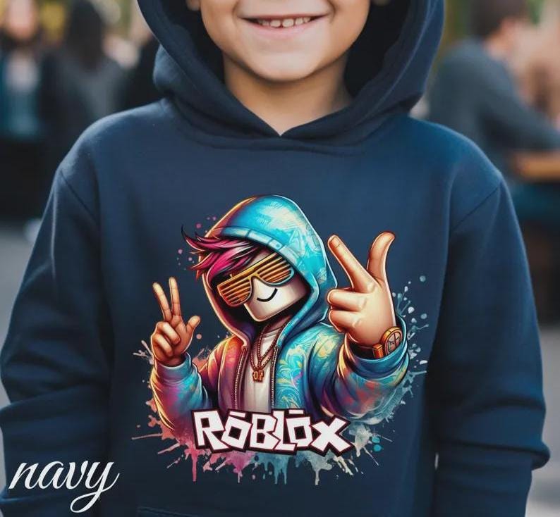 Puede incluir: Sudadera con capucha azul marino con un gr&aacute;fico colorido de un personaje de Roblox con gafas de sol y haciendo el signo de la paz. La palabra "ROBLOX" est&aacute; impresa en blanco y rosa. La palabra "navy" est&aacute; escrita en cursiva en la parte inferior izquierda.