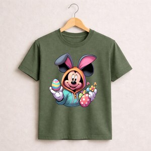 May include: Olive green t-shirt featuring a cartoon Mickey Mouse character dressed as the Easter Bunny. Mickey is holding colorful Easter eggs and flowers. The design includes a hooded sweatshirt and bunny ears.