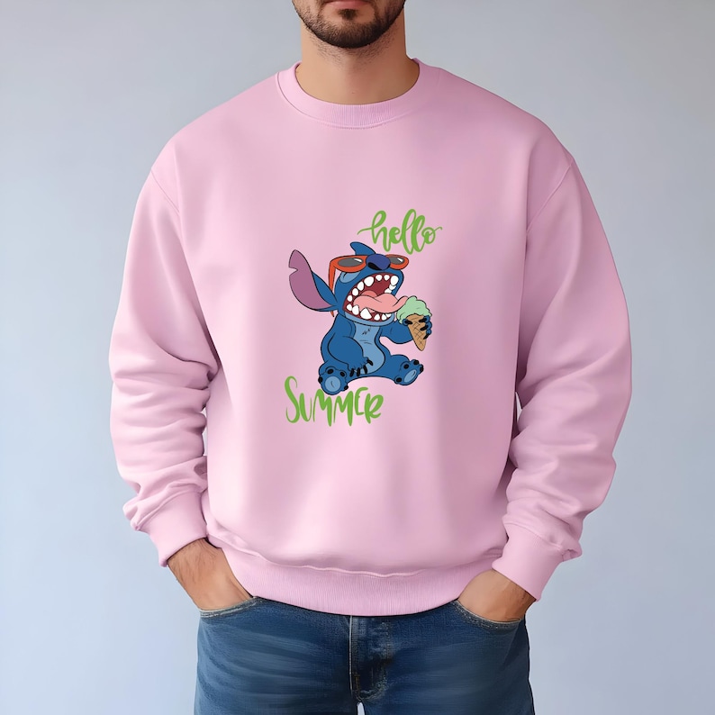 Puede incluir: Sudadera rosa claro con un personaje de dibujos animados azul con gafas de sol y comiendo helado. Las palabras "hello" y "Summer" est&aacute;n escritas en verde. La sudadera es de color rosa liso.