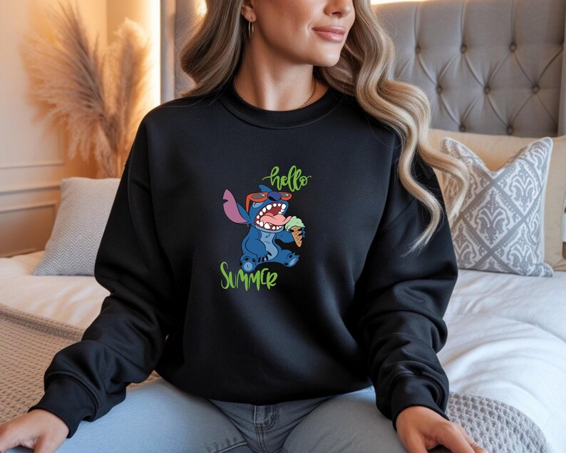 Puede incluir: Sudadera negra con un personaje de dibujos animados de Stitch con gafas de sol y comiendo helado. Las palabras "hello Summer" est&aacute;n escritas en verde arriba y abajo del personaje.