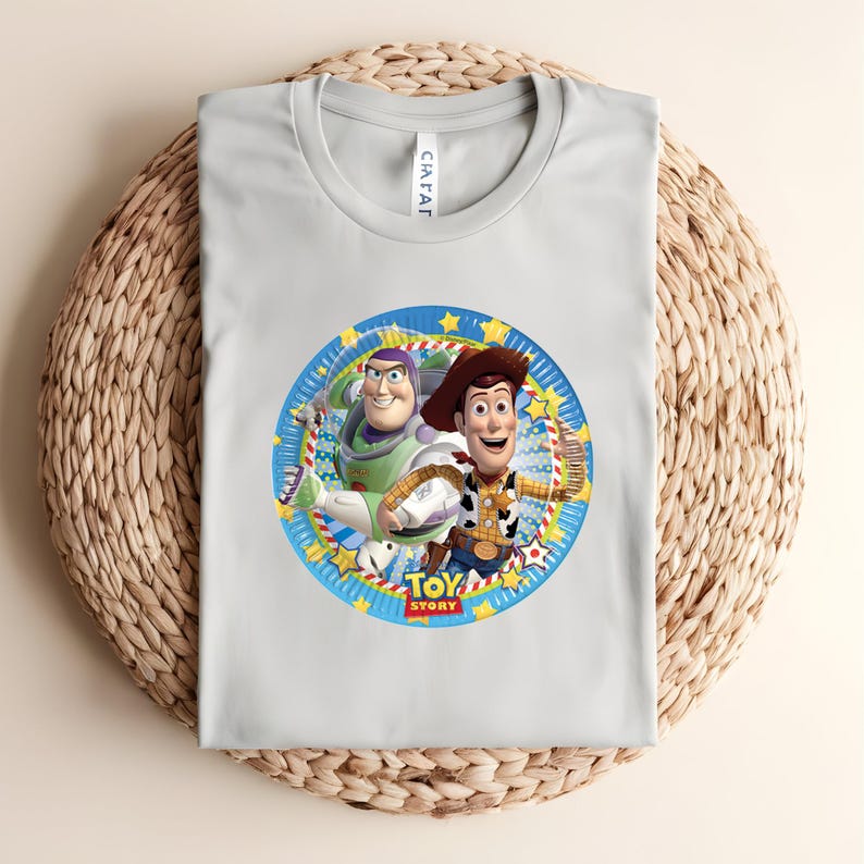 Puede incluir: Una camiseta gris claro con un gr&aacute;fico circular de Buzz Lightyear y Woody de Toy Story. El gr&aacute;fico est&aacute; rodeado por un borde azul con estrellas amarillas y las palabras "TOY STORY".