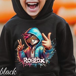 Puede incluir: Sudadera con capucha negra con un gr&aacute;fico colorido de un personaje con gafas de sol y una sudadera con capucha azul, con la palabra "ROBLOX" en blanco y rosa. La palabra "black" est&aacute; escrita en cursiva en la parte inferior.