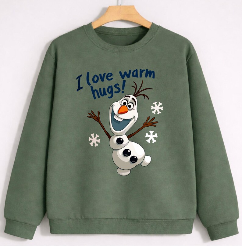 May include: Green sweatshirt featuring a cartoon Olaf character with the text "I love warm hugs!" in blue. The design includes snowflakes. The long-sleeved top is made of a soft material.