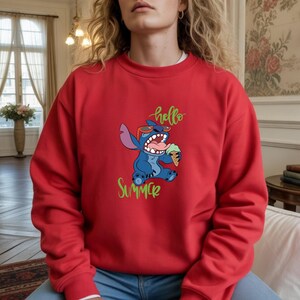 Puede incluir: Sudadera roja con un personaje de dibujos animados azul con gafas de sol y helado. Las palabras "hello Summer" est&aacute;n escritas en verde y amarillo. La sudadera es de color rojo liso.