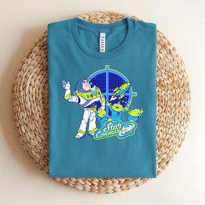 May include: Teal crew neck t-shirt with a graphic of Buzz Lightyear and the Little Green Men from Toy Story. The design includes the words "Star Command" in a stylized font, with a rocket ship and a target.