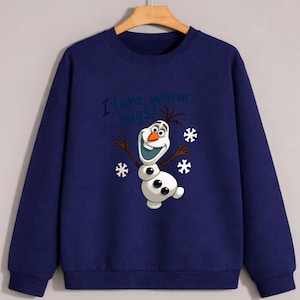 May include: Navy blue sweatshirt featuring a cartoon image of Olaf the snowman with the text "I love warm hugs!". The design includes snowflakes and Olaf's smiling face. The sweatshirt is a comfortable, casual style.