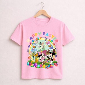 May include: Pink t-shirt featuring a colorful graphic of Disney characters celebrating Easter. The design includes Mickey and Minnie Mouse, Donald and Daisy Duck, and Pluto, surrounded by Easter eggs and the words "Happy Easter".
