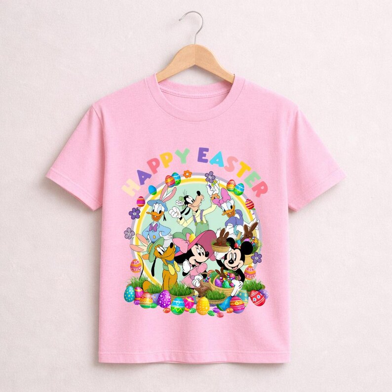 May include: Pink t-shirt featuring a colorful graphic of Disney characters celebrating Easter. The design includes Mickey and Minnie Mouse, Donald and Daisy Duck, and Pluto, surrounded by Easter eggs and the words "Happy Easter".