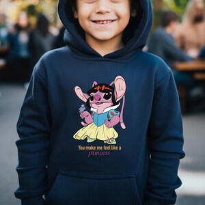 May include: Navy blue hooded sweatshirt featuring a cartoon character dressed as a princess. The character is pink with large ears and is wearing a blue and yellow dress. The text "You make me feel like a princess" is below the graphic.