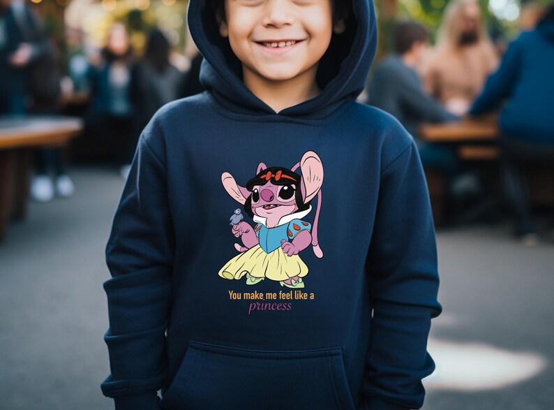 May include: Navy blue hooded sweatshirt featuring a cartoon character dressed as a princess. The character is pink with large ears and is wearing a blue and yellow dress. The text "You make me feel like a princess" is below the graphic.