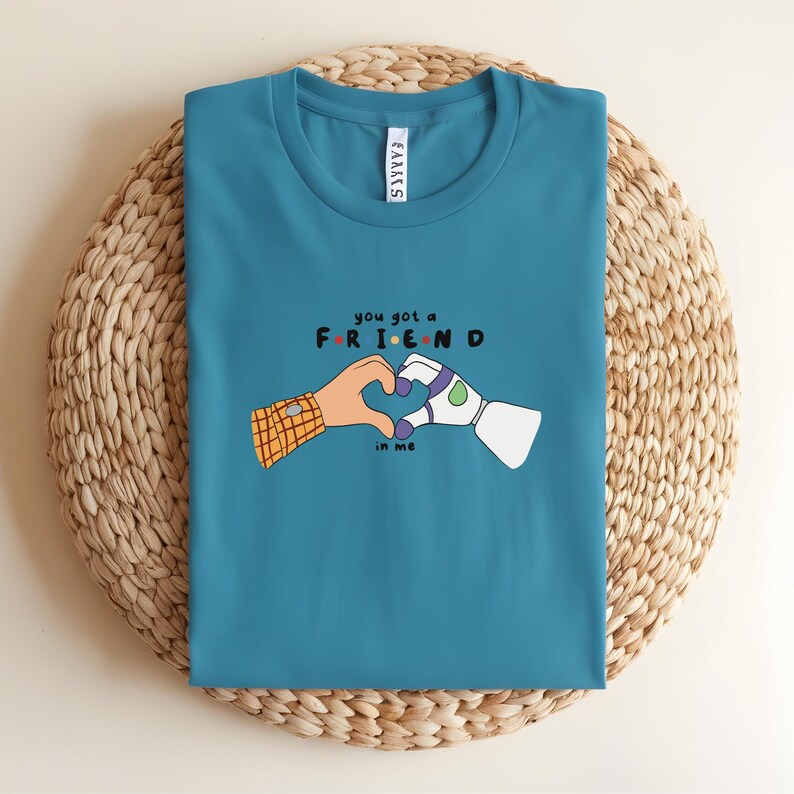 May include: Teal t-shirt with a graphic of two cartoon hands forming a heart shape. One hand is human, the other robotic. The text "you got a FRIEND in me" is above and below the hands.