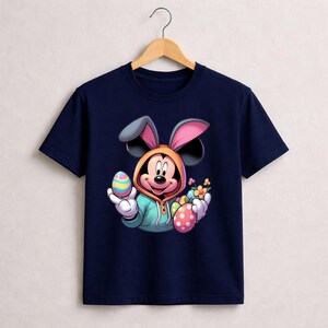 May include: Navy blue t-shirt featuring Mickey Mouse dressed as a bunny holding Easter eggs and flowers. The cartoon character wears a hooded sweatshirt with bunny ears. The eggs are colorful with polka dots and stripes.