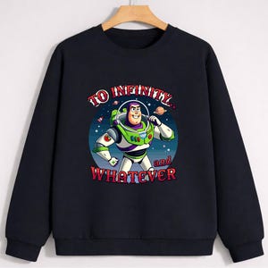 Op de afbeelding: Zwarte sweatshirt met een afbeelding van Buzz Lightyear uit Toy Story. Het ontwerp bevat de zin "TO INFINITY... and WHATEVER" in een kleurrijk, gestileerd lettertype. Buzz is afgebeeld in zijn ruimte ranger pak.